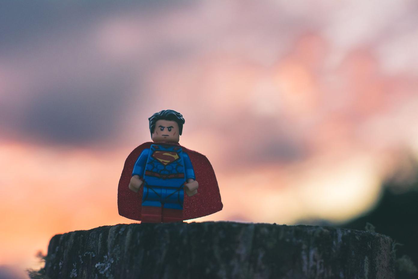Lego Superman figure standing on a cliff overlooking a cloudy sunset